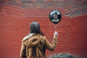 Someone stands and is clearly inspired as they hold a balloon with motivational writing on it "Up To You" 